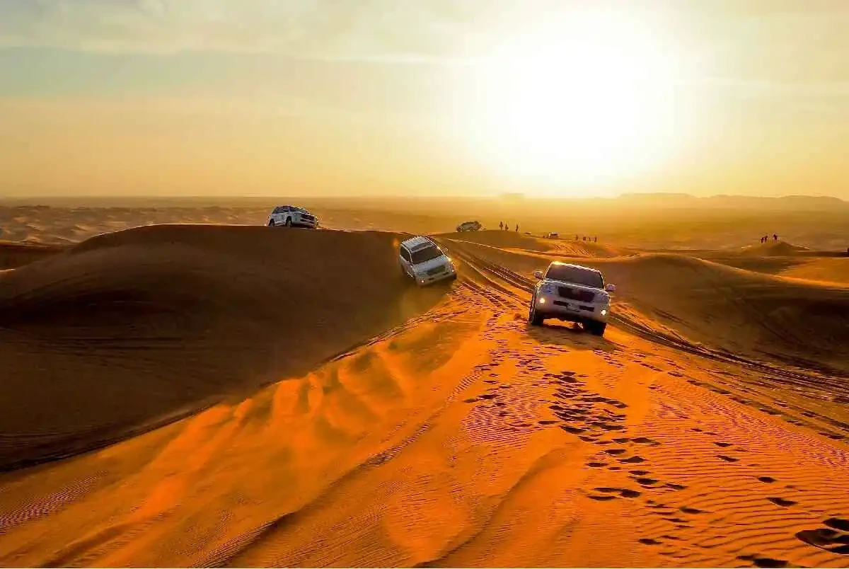 Four 4x4 vehicles driving through a desert landscape at sunset during an overnight safari adventure.