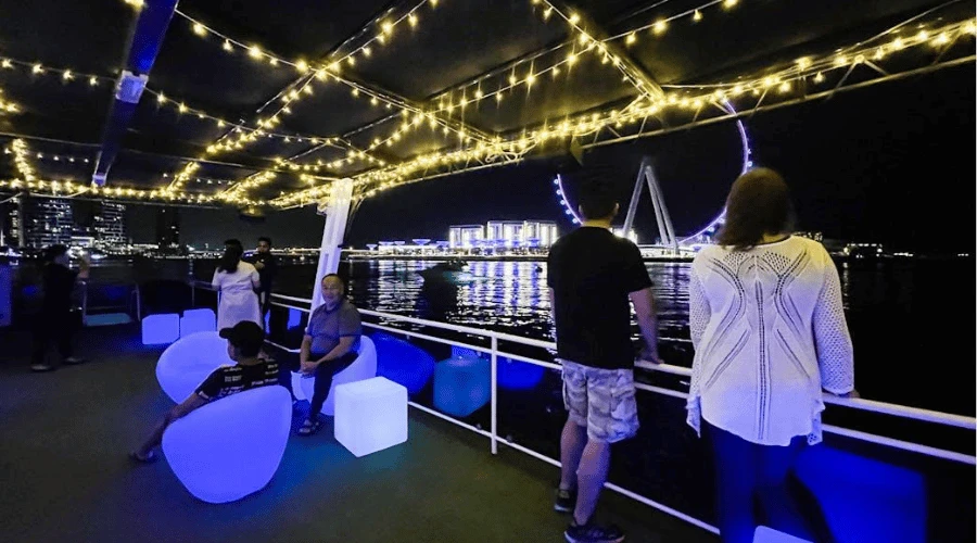 Sightseers relaxing on the cruise lounge deck with panoramic nighttime views of Ain Dubai on Bluewaters Island.