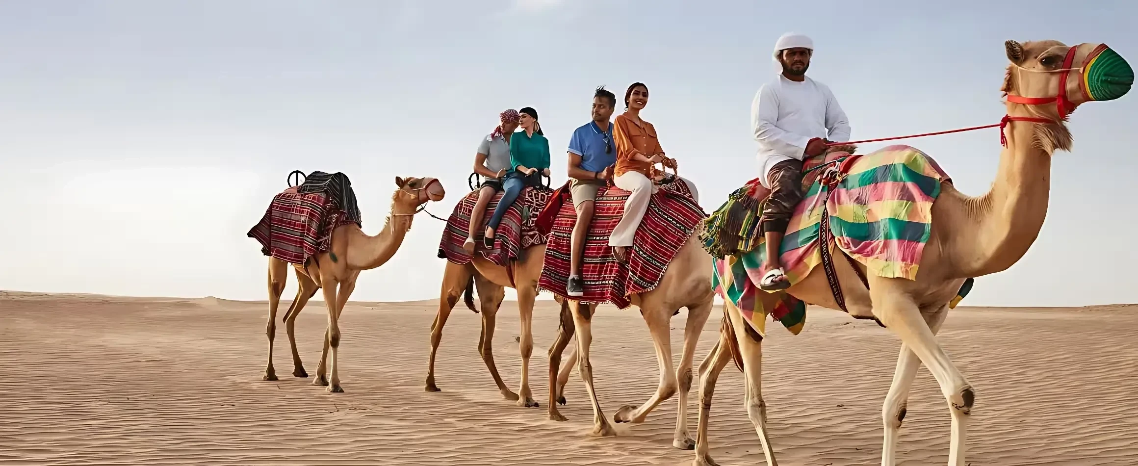 Tourists enjoying a guided camel ride across the desert during an Al Ain city tour from Dubai