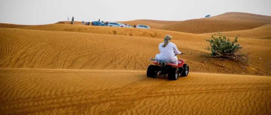 A man on an ATV navigating through the arid desert terrain, surrounded by sand dunes.