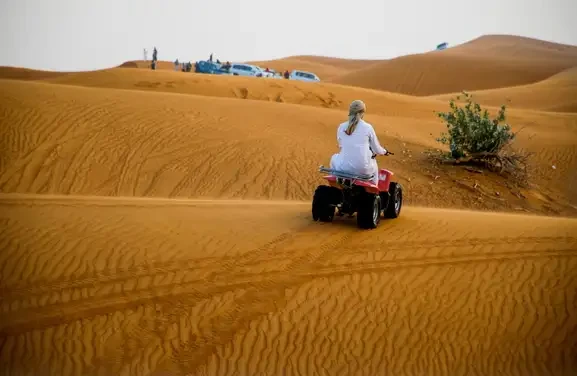 A man on an ATV navigating through the arid desert terrain, surrounded by sand dunes.