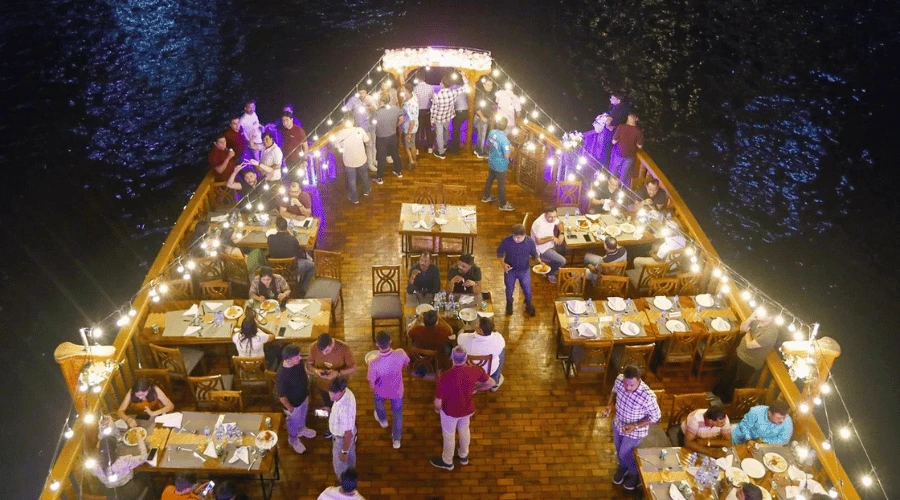 Guests enjoying dinner and fairy lights on the open wooden upper deck of a Dubai Marina dhow cruise.