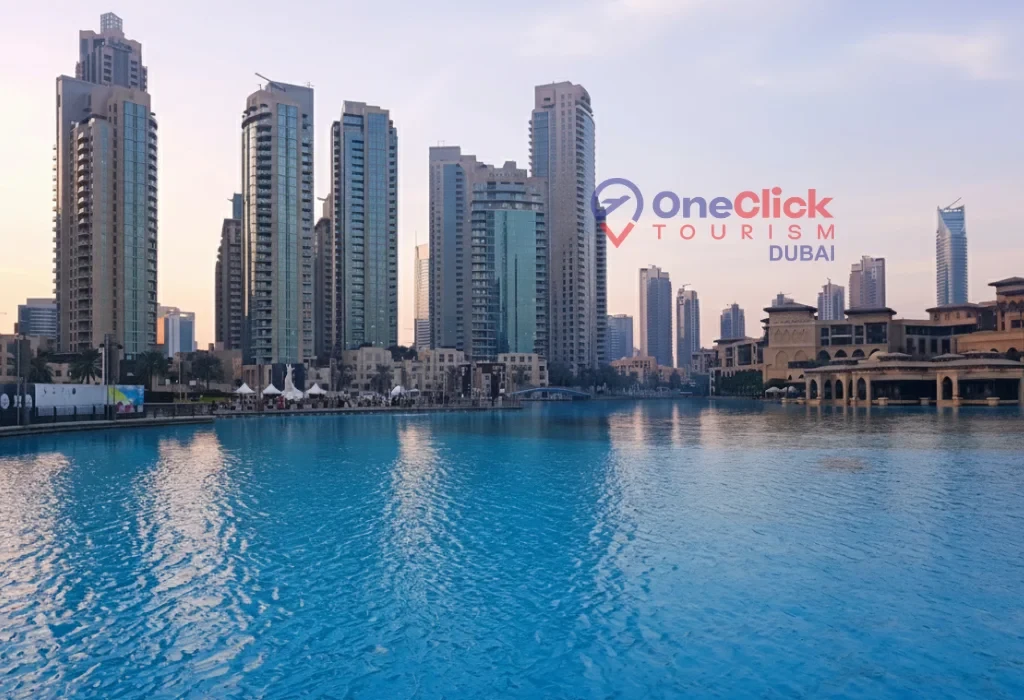 Wide view of the blue Burj Khalifa lake surrounded by luxury skyscrapers in Downtown Dubai at sunset.