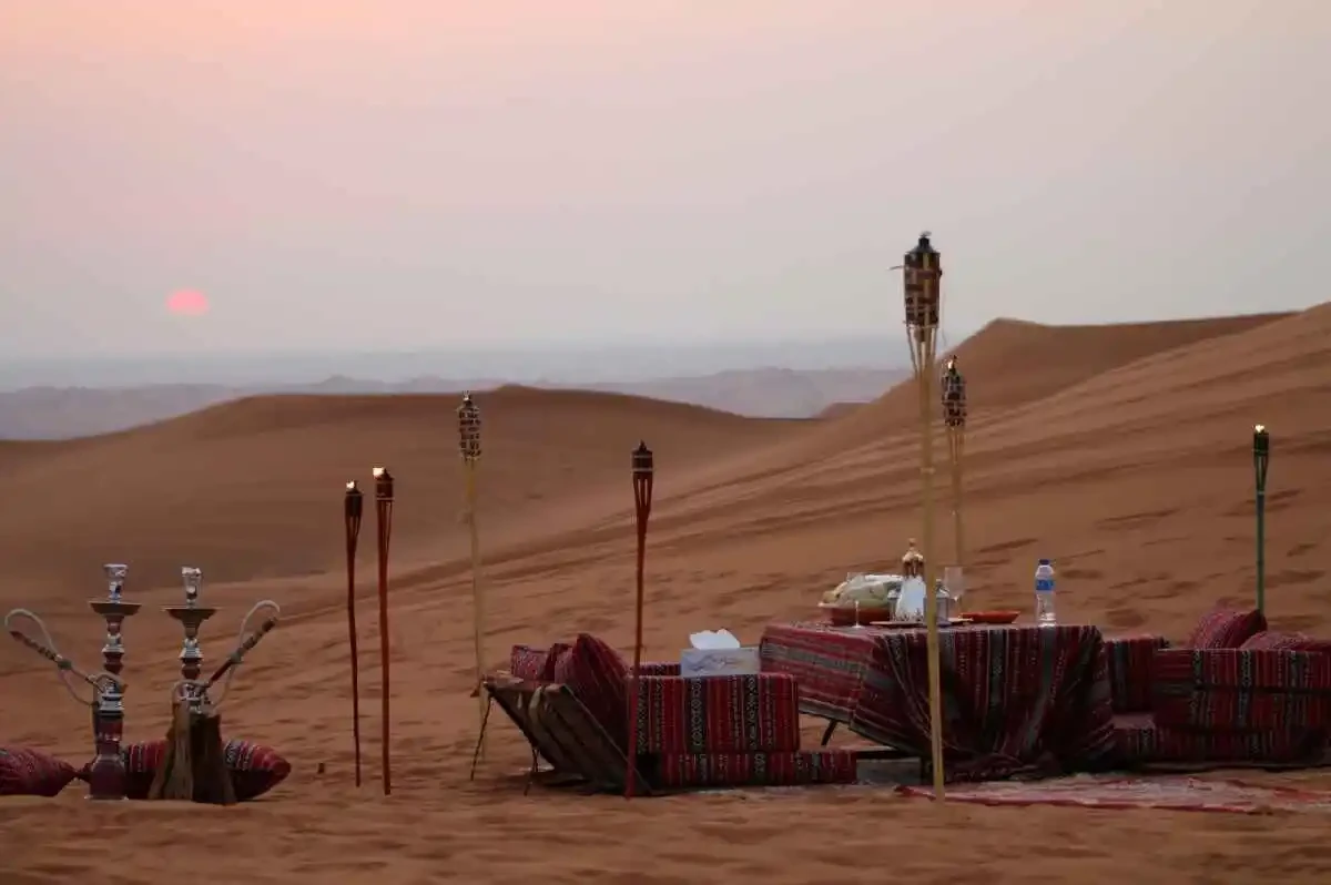A beautifully arranged dinner table in the desert at sunset, complete with a hookah, evoking a tranquil ambiance.