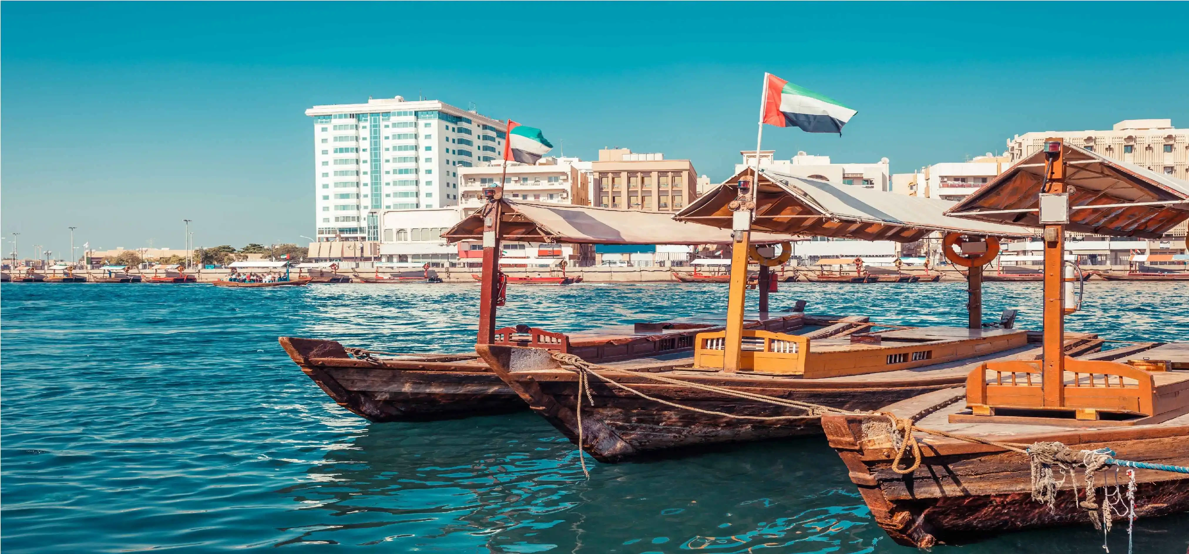 Two boats are docked in Dubai Creek, gently bobbing in the water under a clear sky.