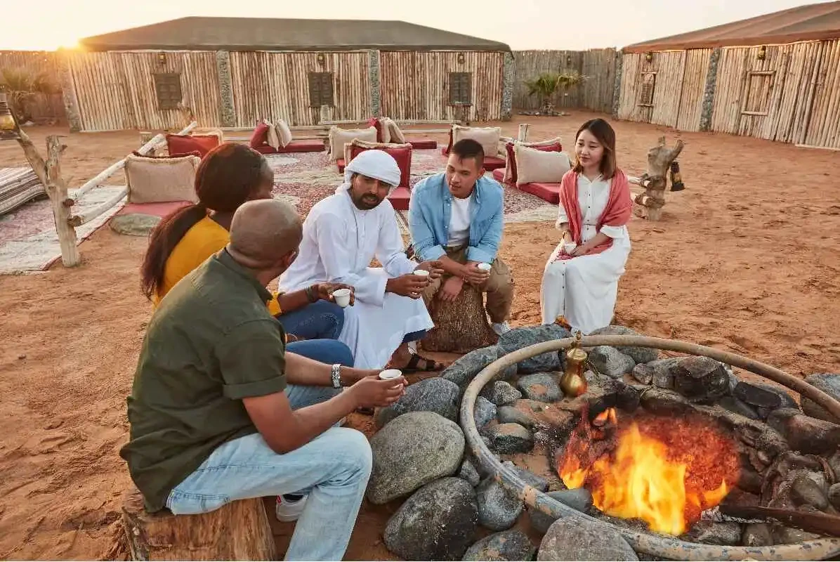 Five people gathered around a fire pit, enjoying a cozy evening in a desert camp setting.