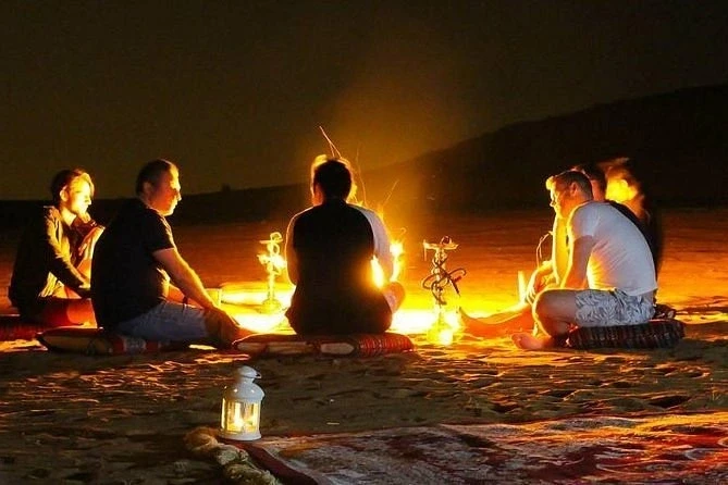 A circle of individuals around a fire on the beach, enjoying discussions during their overnight safari adventure.