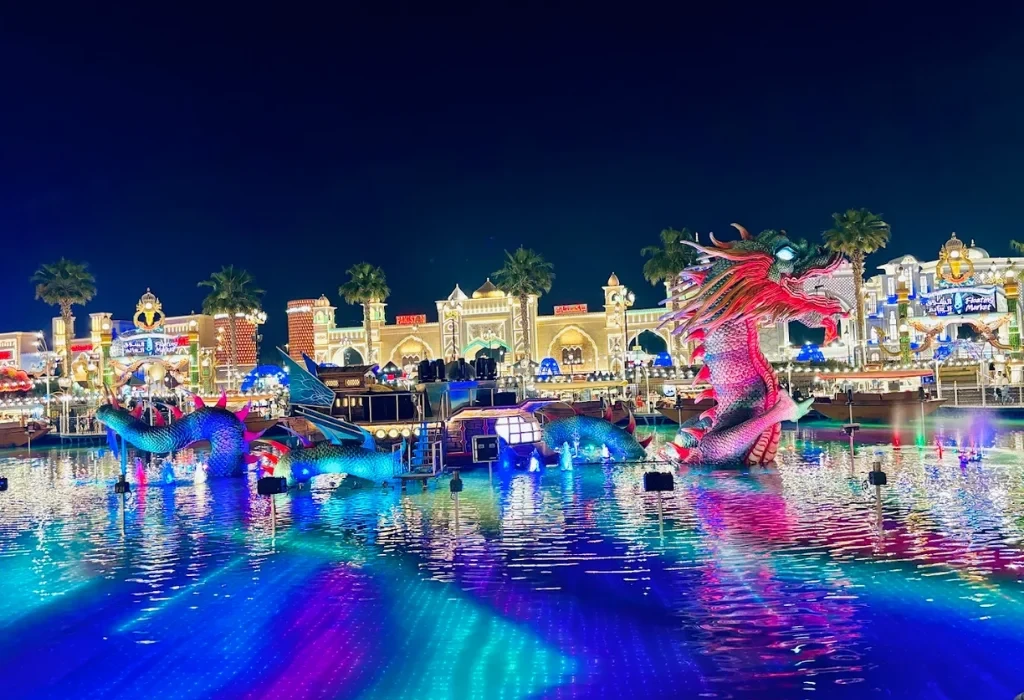 Large illuminated dragon sculpture at the Global Village Dubai floating market reflected in the water at night.