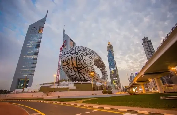 A large sculpture of a giant snake prominently displayed outside a museum in Dubai, surrounded by urban architecture.