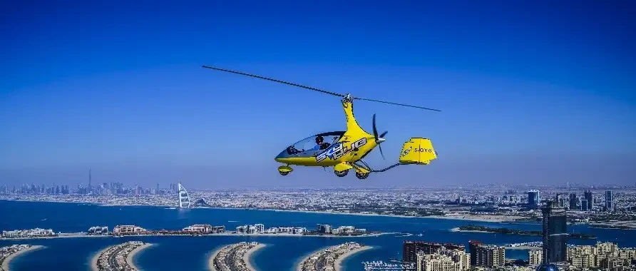 A helicopter flies over Dubai, showcasing the city skyline in the background against a clear blue sky.