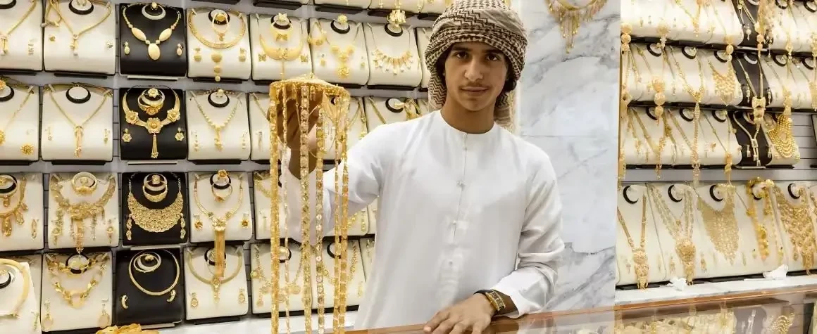 Local shopkeeper in traditional attire displaying gold items