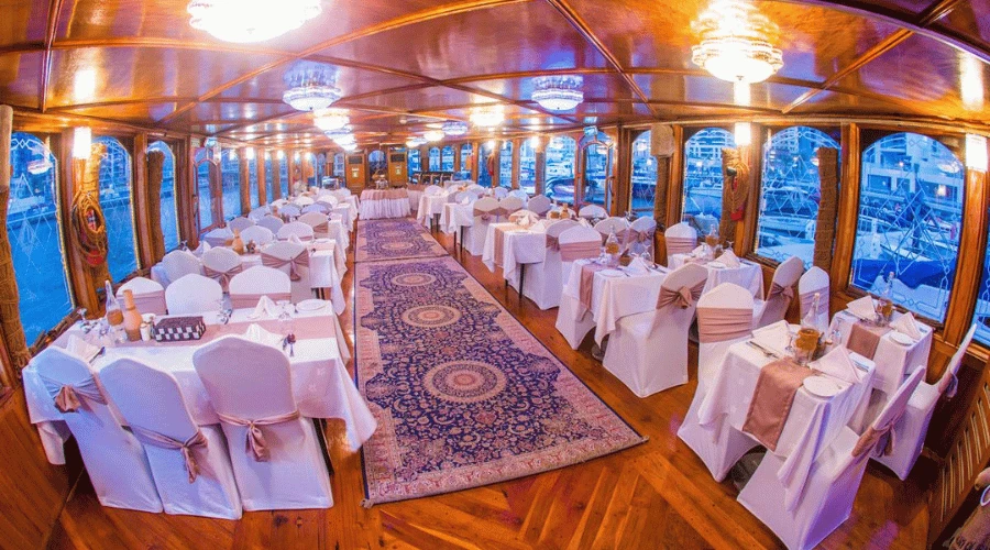 Fully air-conditioned lower deck dining hall with traditional oriental carpet and glass-window views in Dubai Marina.