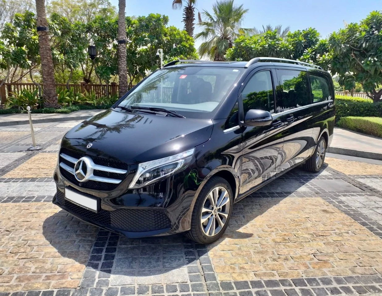 Front angle of a black Mercedes V-Class van on a cobblestone driveway, ideal for luxury chauffeur services in Dubai.