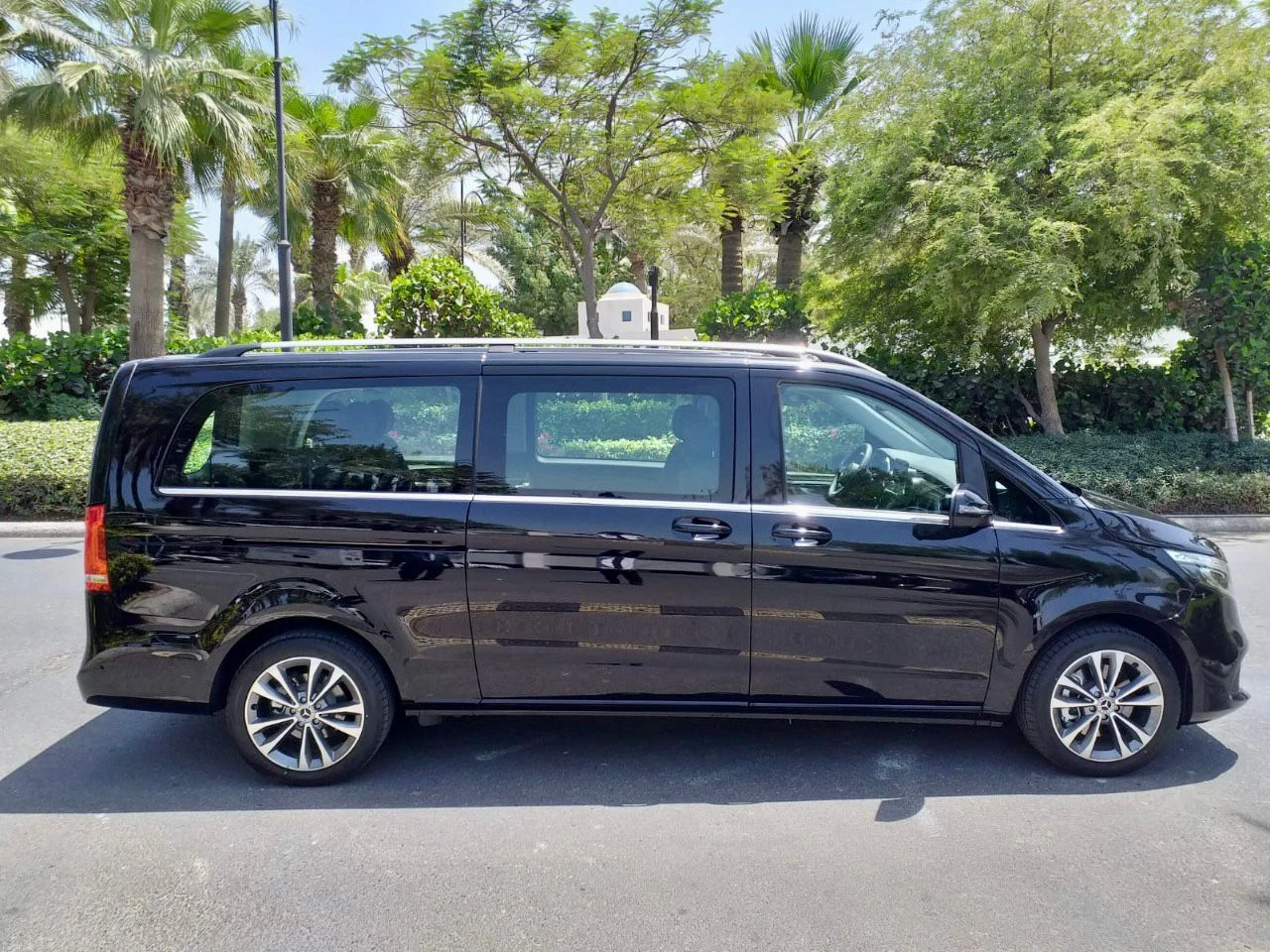 Side view of a luxury black Mercedes-Benz V-Class parked in a tropical Dubai setting with palm trees.