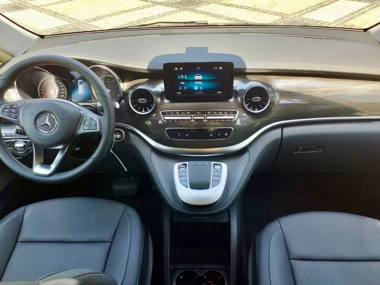 Interior dashboard of a Mercedes V250 rental featuring the steering wheel, infotainment screen, and premium wood trim.