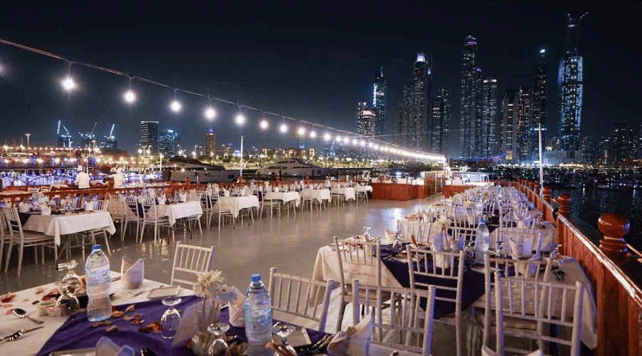 Elegant outdoor dining table setup with white linens on the deck of a Dubai Marina dinner cruise overlooking nighttime towers.