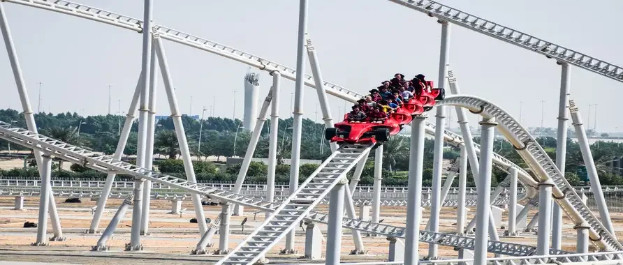 Children laughing and screaming on a roller coaster ride at an amusement park, surrounded by colorful attractions.