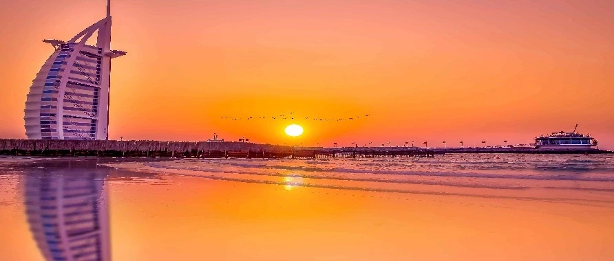 The sun sets behind the Burj Al Arab hotel, casting a warm glow over the iconic structure in Dubai.