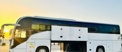 A white 16-50 seater bus parked in front of a building, available for rent in Dubai and Abu Dhabi.