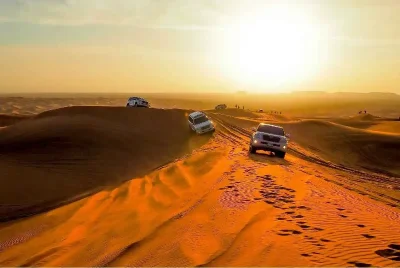 Four 4x4 vehicles driving through a desert landscape at sunset during an overnight safari adventure.