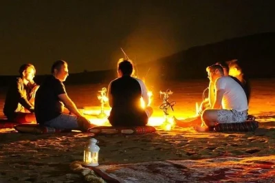 A circle of individuals around a fire on the beach, enjoying discussions during their overnight safari adventure.