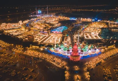 Wide panoramic shot of the Global Village Dubai park at night featuring glowing architectural structures and colorful lights.