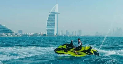 A man riding a yellow and black jet ski across the ocean waves under a clear blue sky.