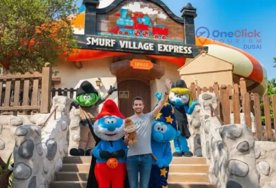 Two Smurf mascots in blue and red outfits performing for guests at the Smurfs Village zone in Motiongate Dubai.