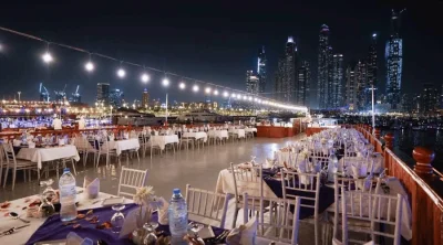 Elegant outdoor dining table setup with white linens on the deck of a Dubai Marina dinner cruise overlooking nighttime towers.
