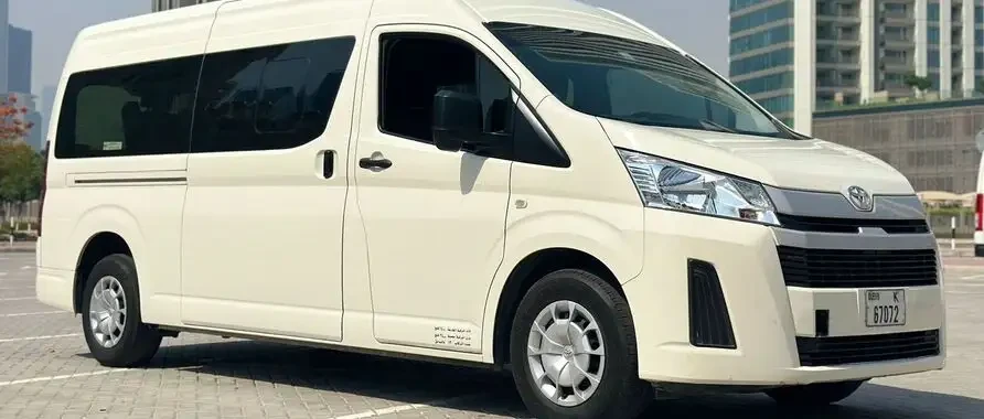 A white van, a Toyota Hiace 13-seater, parked in a parking lot, ready for rental in Dubai and Abu Dhabi, UAE.