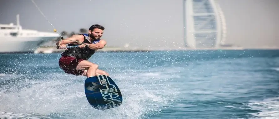 A man wakeboards in the ocean, with a boat visible in the background, showcasing an exciting water sport activity.