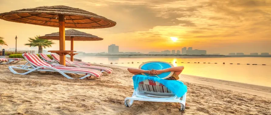 A woman sits comfortably in a beach chair with a hat and umbrella, enjoying the beach at an Abu Dhabi attraction.